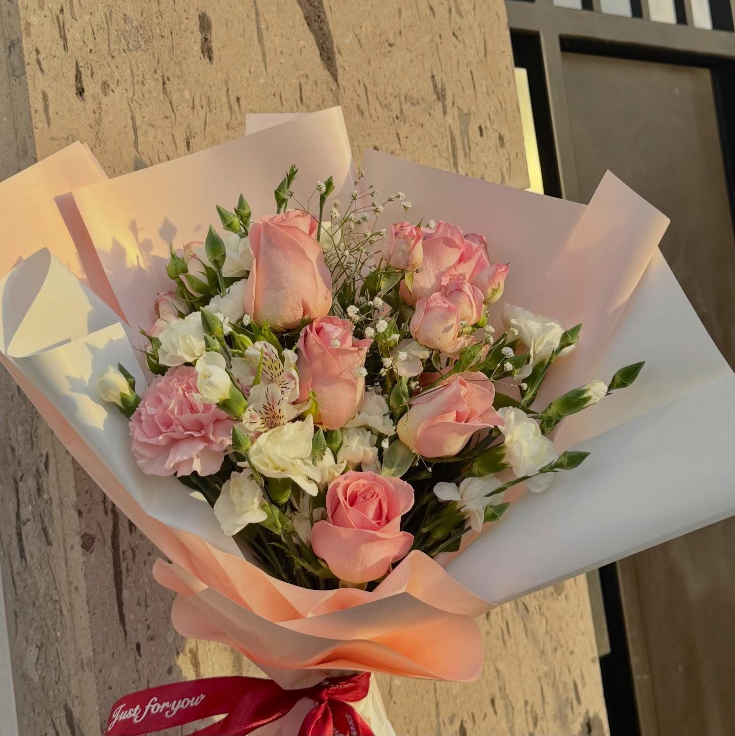 Ramo de rosas rosadas y flores blancas envuelto en papel rosa
